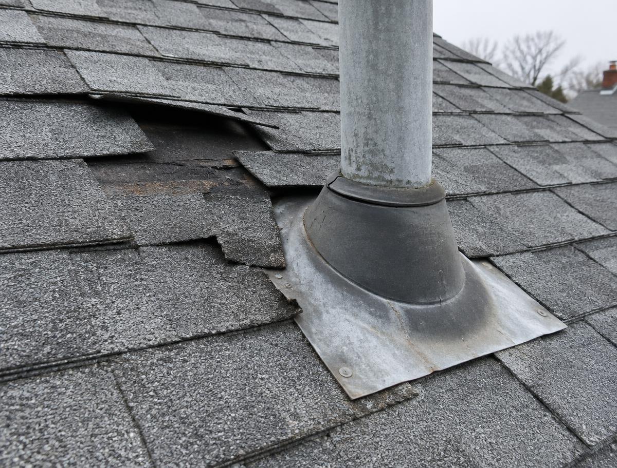 Damaged shingles beside a roof vent flashing